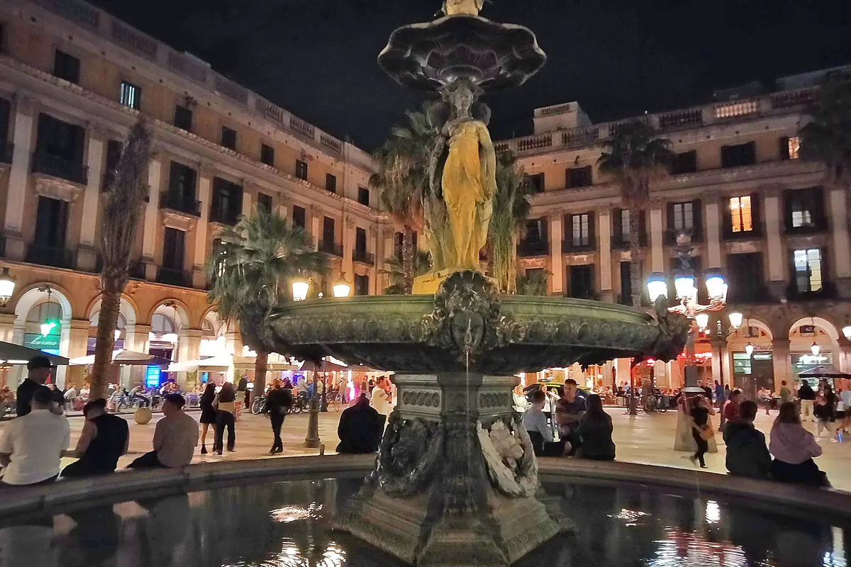Fontána Tří grácií uprostřed Plaça Reial v noci, nasvícená zdola, v pozadí budovy s arkádami