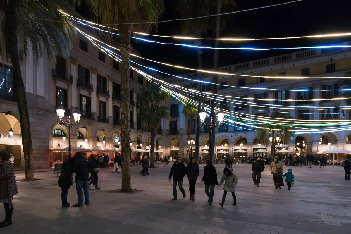 Plaça Reial at night, with strings of lights stretched between palm trees over a square of street lamps and arcaded buildings